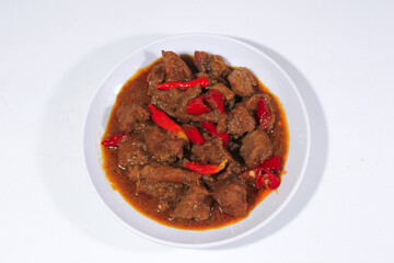 beef cooked in spicy spices with chili garnish on top, served on a white plastic plate