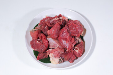 Fresh beef is cut into cubes and served on a white plate covered with banana leaves