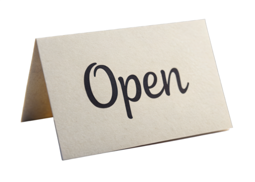 A close-up shot of a simple white open sign card isolated on a white background. The card has a folded, triangular base for easy placement and the word Open is written in black, cursive text. Generati