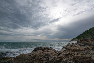 Waves crash against a rocky shoreline with mountains in the background