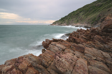 Waves crash against a rocky shoreline with mountains in the background