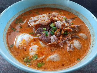 Thai spicy noodle soup with pork and egg on wood table
