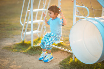 baby girl with happy time in outdoor by swing play on grasses floor in blue dress