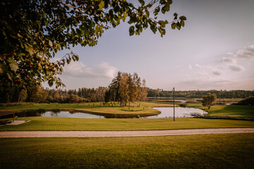 Blome, Latvia - September 11, 2023 -  Scenic park landscape with a pond, lush greenery, trees, and a clear sky, framed by overhanging branches. Copy space.