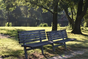Fototapeta premium Two wooden benches on a riverside meadow in the morning