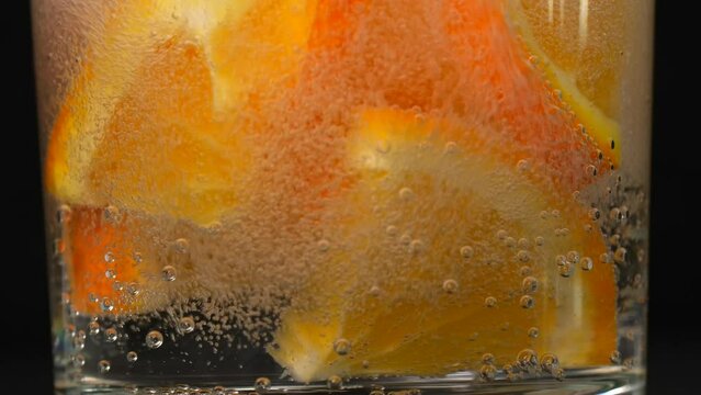 Orange slices plummet into glass of sparkling water closeup. Burst of bubbles erupts around adding zesty visual pop to fizzy drink