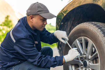 Asian automobile mechanic repairman wearing uniform and protection glove screwing the wheel with a wrench in workshop. Car service and maintenance, Repair service.