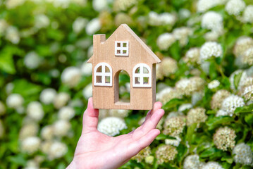 The girl holds the house symbol against the background of white flower
