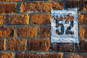 Weathered black and white 52 house number painted on an orange brick wall
