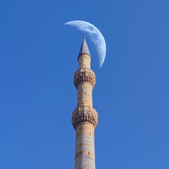 Obraz premium front view, Very tall mosque minaret, blue sky background, a curved moon in the sky
