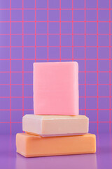Stacked pastel soaps, trendy and modern, against neon purple-pink tiles.