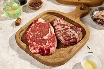 Raw New York Strip and Chuck Roll Steaks on Wooden Board in Summer Sunlight