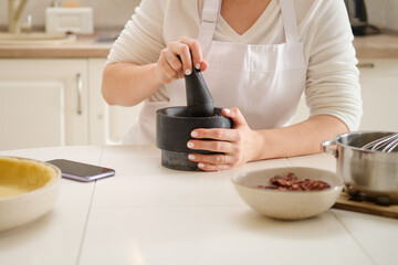 Woman using mortar and pestle while making pecan pie. Process of cooking pecan pie in home kitchen for American Thanksgiving Day.