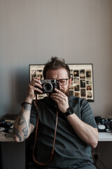 Hipster photographer taking pictures with a retro-style film camera in a home studio environment.