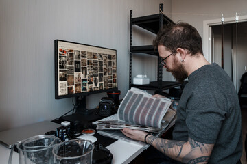 A photographer reviews film negatives beside a digital editing setup, showcasing a blend of modern technology and traditional photography methods.