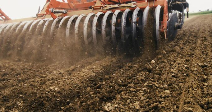 Super slow motion of modern agricola machinery tractor with disk plow harrows cultivates field and prepares land soil for sowing in ecological rural farmland agricultural plantation at 1000 fps.