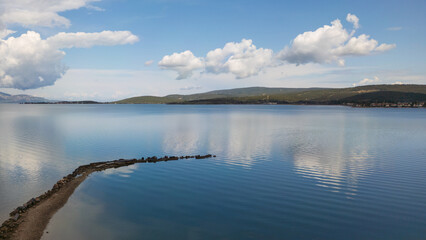 A stunning natural landscape of a large lake with mountains in the background, reflecting clouds in the water under a beautiful sky