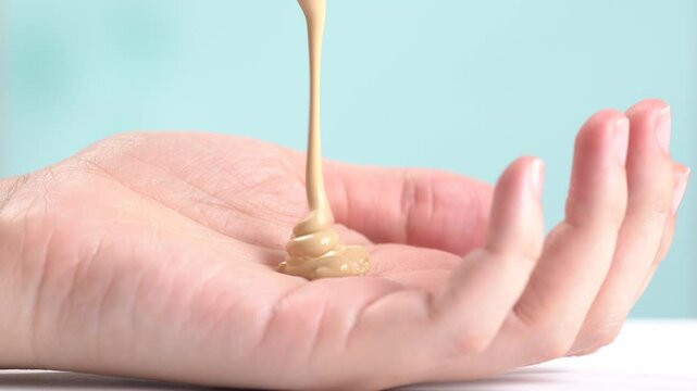 Pouring skin foundation onto palm of hand on blue background. Decorative cosmetics advertising concept.