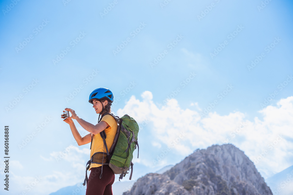 Wall mural climber on top of the mountain takes a photo. girl with a backpack and hard hat in the mountains. wo