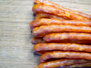 A series of meat sticks rest on a wooden table, slim and consistent in hue, arranged tidily in a straight line, suggesting they are ready to be eaten.