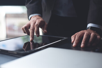 Businessman manager using digital tablet, finger touching on tablet screen, browsing the internet with laptop computer on table, close up. Business man working on computer at modern office