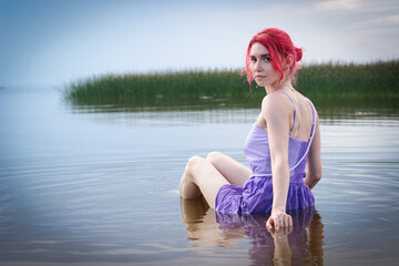 Beautiful girl in a dress poses in the water against the background of nature