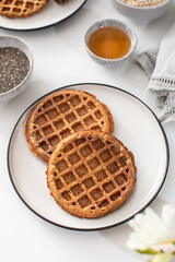 Homemade oatmeal and chia seed waffles on a white plate, accompanied by honey and ingredients