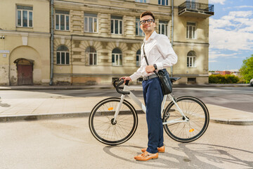 Obraz premium A young businessman, standing confidently with his bicycle and leather shoulder bag in an urban environment.