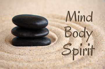 Mind, body and spirit text with black Zen stones on sand background
