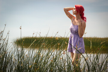Beautiful girl in a dress poses in the water against the background of nature