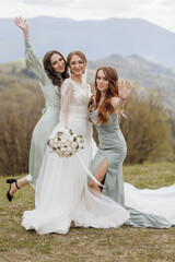 Three women are posing for a photo on a grassy hillside. One of the women is wearing a wedding...