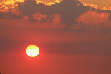 Sunset with clouds. View of the red disk of the sun among the clouds descending down.