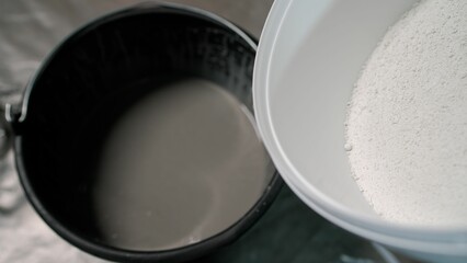 Adding hardener to a bucket of plaster. The white solution is poured into a bucket.