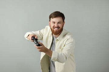 Happy man playing video game with controller on grey background