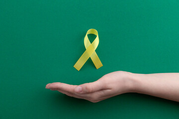 Woman with yellow awareness ribbon on green background, top view. Space for text