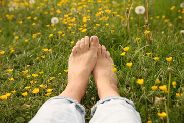 Woman sitting barefoot on green grass outdoors, closeup