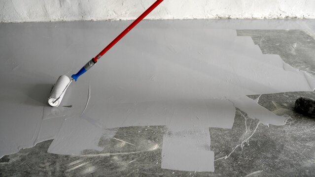 Varnishing of concrete floors. Apply primer to the surface using a roller brush. Close-up. Applying paint with a roller to a concrete floor. A man paints a concrete floor with a paint roller.