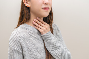Sickness in inflaming asian young woman, girl use hand check self touch at sore throat, pain thyroid gland on neck or disease reflux, acid of suffer people on wall background. Medical and healthcare.