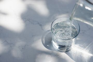 Pouring drinking water into glass on white marble table.