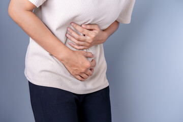 Young woman holding hands on stomach, suffering from severe abdominal pain feeling extremely unwell Menstrual pain Stomach pain from food poisoning, stomach pain, and digestive problems.