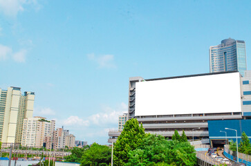 A mockup of a blank white billboard framed by shopping mall building facade under a clear blue sky in Soul city,ideal for advertising