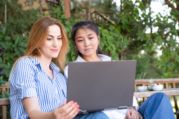 Happy young multiethnic couple spending time together at the park, studying while with laptop