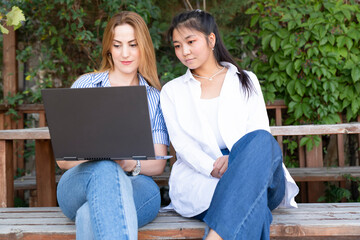 Happy young multiethnic couple spending time together at the park, studying while with laptop