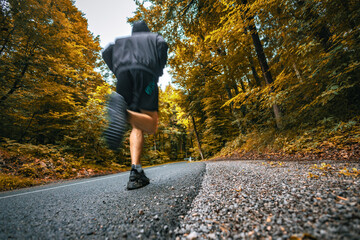 Right behind shot of a young male runner running on an asphalt road in autumn season.