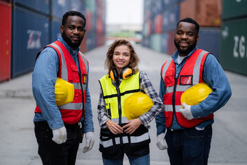 Three people wearing safety gear and holding hard hats. One of them is smiling. The scene is set in a warehouse or construction site