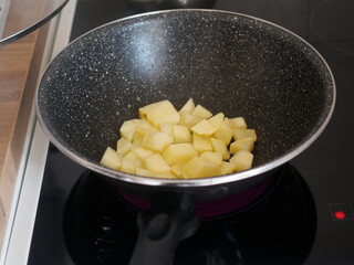 Diced potatoes in a wok pan sitting on a stovetop
