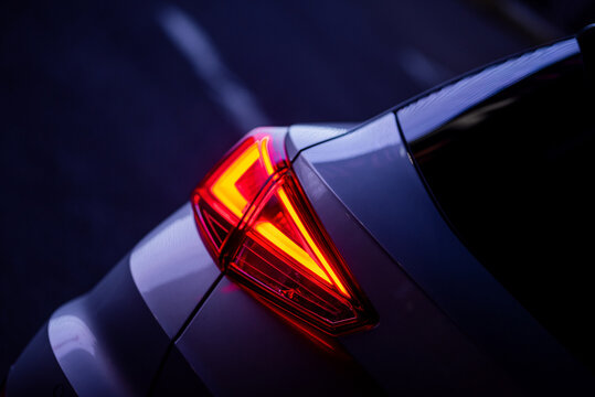 Illuminated triangular tail light at night. Diagonal close-up image of compact hatchback in violet light. Reflection of city lights in the cars bodywork. 