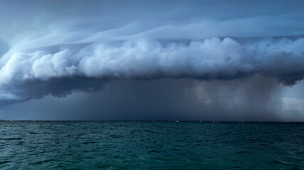 A dramatic cloud formation over the ocean, signaling an approaching storm, with dark and turbulent waters underneath.
