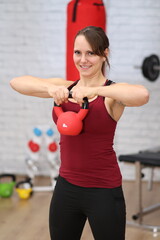 junge Frau schwingt Kettleball in Brusthöhe, lächelt, Seitenansicht
