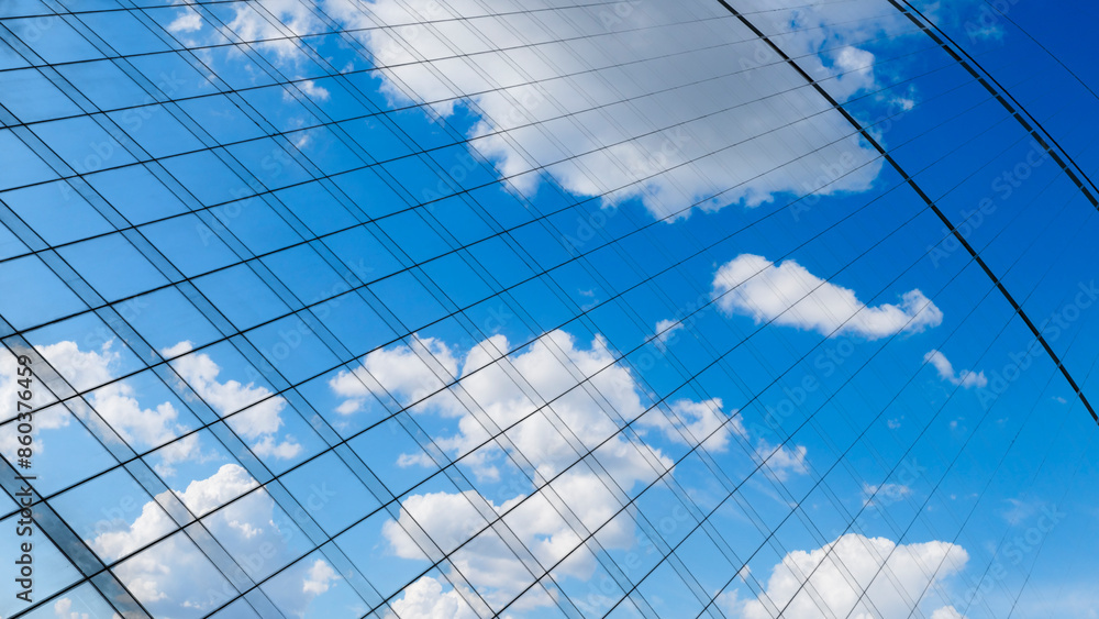 Poster reflection of a blue sky with white clouds on the glass wall of a skyscraper in the business center 
